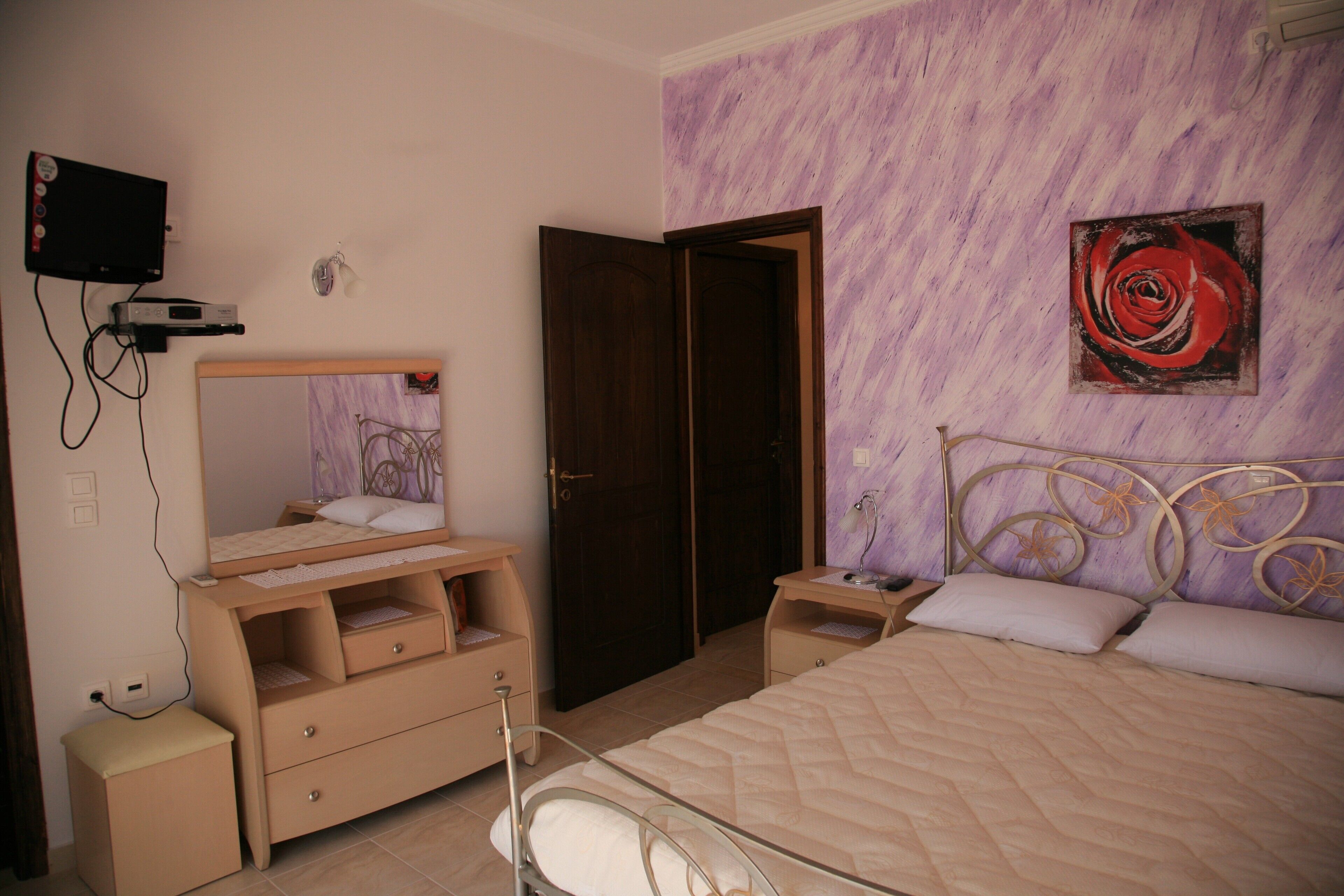 A bedroom with a bed, bedside tables, a dresser, a TV, and a door.