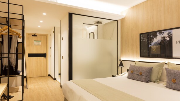 A modern hotel room with a bed, a walk-in closet, a shower, and a large mirror.