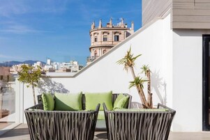 Un balcón con mobiliario de mimbre y vista a un edificio histórico.