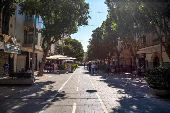 A pedestrian street lined with trees and outdoor seating areas, with buildings on either side.