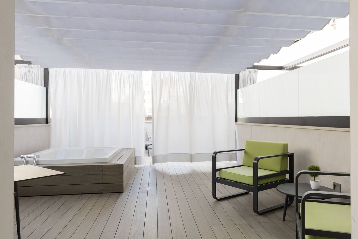 Un espacio exterior moderno con zona de estar, un deck de madera, una silla verde con cojín, una mesita y una planta en maceta.