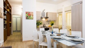 A modern kitchen with white cabinets, a stainless steel range hood, and a dining area with a glass table and white chairs. - House Gregorio, large and comfortable apartment (Roma)