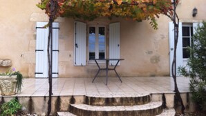 Un bâtiment doté d’un patio couvert, de volets blancs et d’une plante en pot.