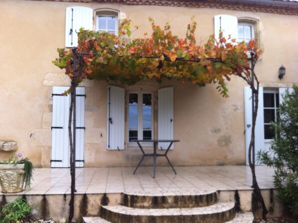 A building with a covered patio area, white shutters, and a potted plant.