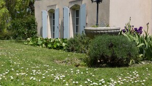 Un bâtiment avec un jardin à l’avant, agrémenté d’un jardinier en pierre, de fleurs blanches et de feuillage vert.