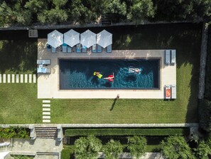 An aerial view of a swimming pool area with a rectangular pool, lounge chairs, and umbrellas.