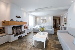 A spacious living room with a fireplace, a sofa set, a coffee table, and a dining area in the background.