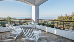 Een balkon met witte stoelen en een tafel, met uitzicht op een schilderachtig zeegezicht en groen.