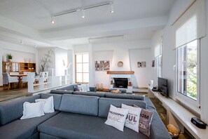 A spacious living area with a grey sectional sofa, a fireplace, and a dining area with a white table and chairs.