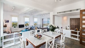 Een ruime woonkamer met een groot raam met uitzicht op zee, een eethoek met een marmeren tafel en een gezellige zithoek met een panorama.