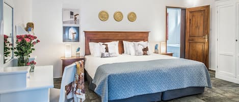 A hotel room with a large bed, a desk with a chair, a wooden wardrobe, and a mirror.