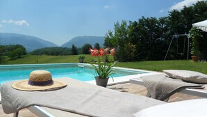 Uma área à beira da piscina com espreguiçadeiras, um chapéu e um vaso de planta.