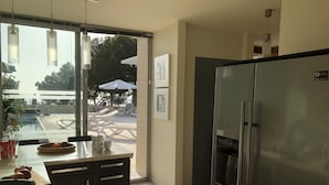 A modern kitchen with a stainless steel refrigerator, a dining area with a table and chairs, and a view of an outdoor pool area. - Superb location & views, heated pool (Apr - Oct), beach/restaurants 7 mins walk! (Almunecar)