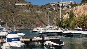 A marina with multiple boats docked, surrounded by rocky hills and a few buildings in the background. - Superb location & views, heated pool (Apr - Oct), beach/restaurants 7 mins walk! (Almunecar)