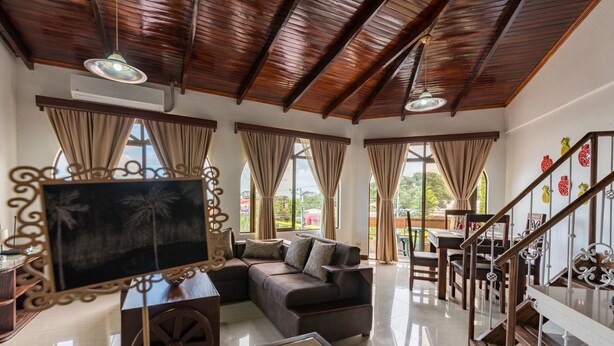 A spacious living area with a wooden ceiling, a large flat-screen TV, a sofa, and a dining table. - Los Arcos dowtown 🌋🌋 (La Fortuna)