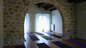 Habitación de paredes de piedra con un arco de entrada, colchonetas de yoga en el suelo y vista a través del arco.
