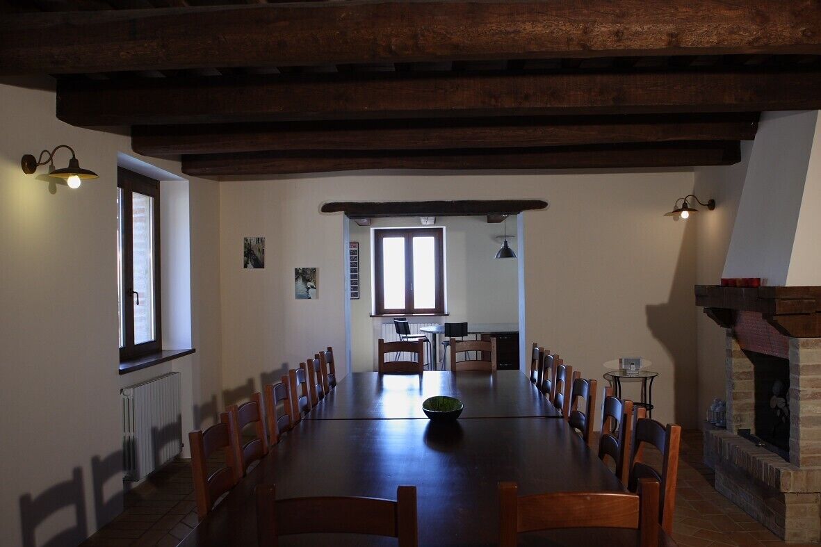 A long dining table with chairs, a fireplace, and a kitchen area in the background.