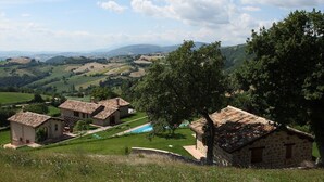 Un paisaje rural con edificios de piedra, una piscina y colinas ondulantes al fondo.