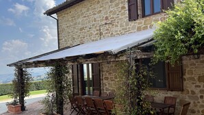 Un edificio de piedra con un patio cubierto, mesas al aire libre y plantas en macetas.