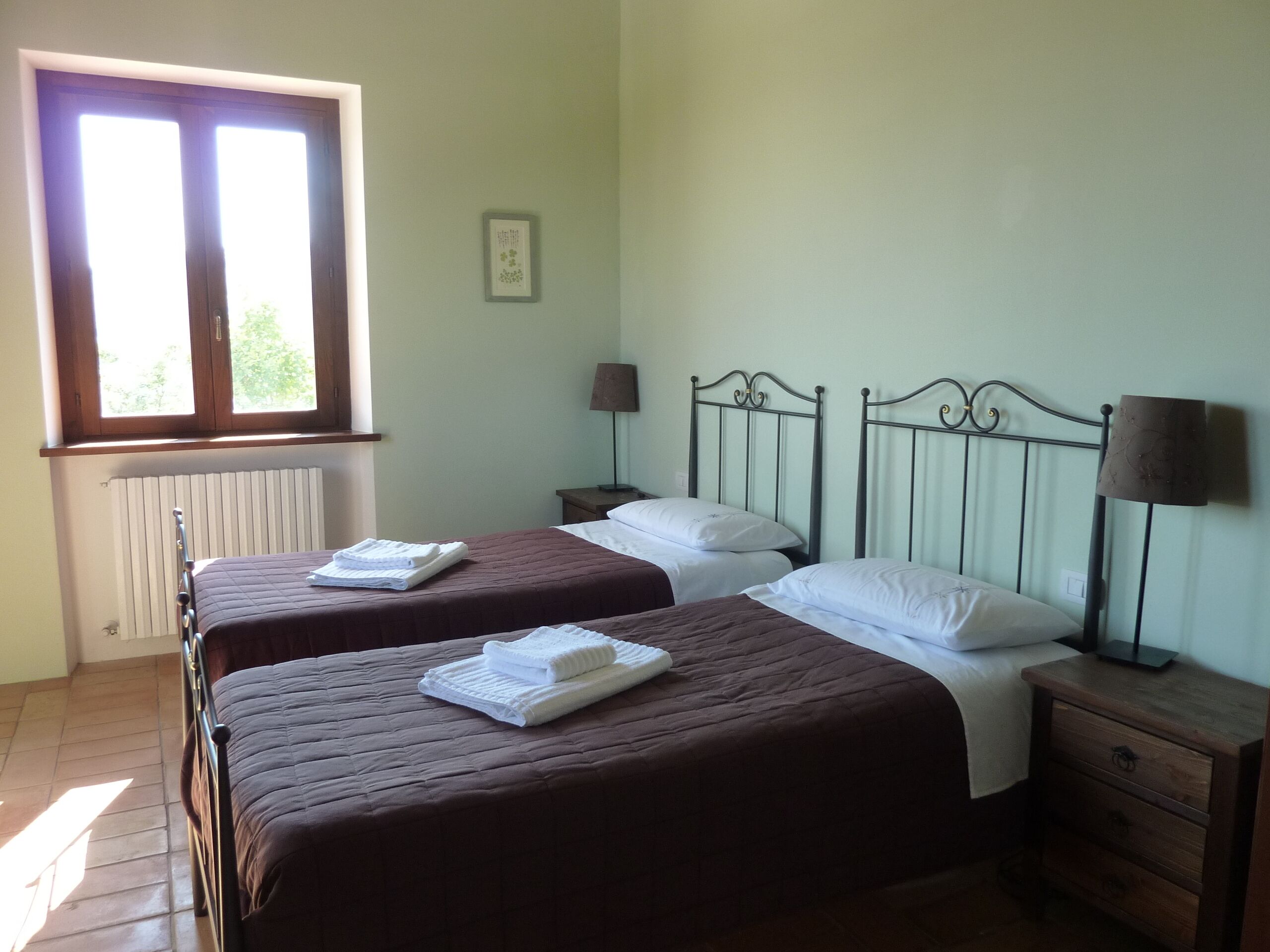 Ein Schlafzimmer mit zwei Betten, einem Fenster, einer Heizung und einem Nachttisch mit Lampe.