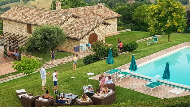 Una villa con piscina, mobiliario exterior y un edificio de piedra con tejado de baldosas.