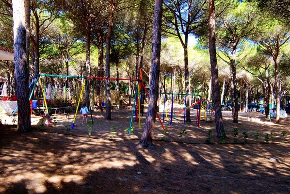A playground with swings and climbing structures surrounded by trees. - Happy Camp in Camping Bella Sardinia (Cuglieri)