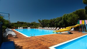 A wooden deck with a swimming pool, lounge chairs, and a water slide. - Happy Camp in Camping Bella Sardinia (Cuglieri)