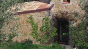 Um edifício de pedra com telhado vermelho, rodeado por vegetação e com vista para a costa.
