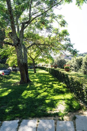 A tree-lined pathway with a hedge, a paved area, and a distant view of buildings. - Luxury apartment with pool: dolce vita at 15' on foot from the heart of Siena! (Siena)
