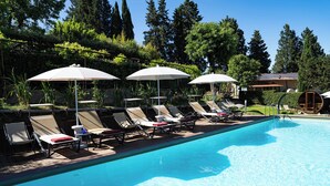 A swimming pool with lounge chairs and umbrellas, surrounded by greenery and trees.