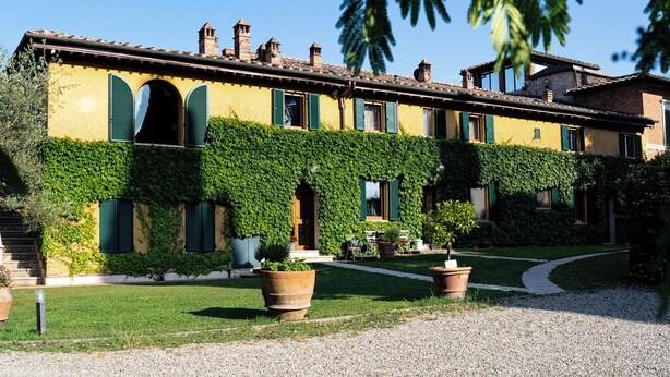 A building with a yellow facade, green shutters, and a gravel driveway.