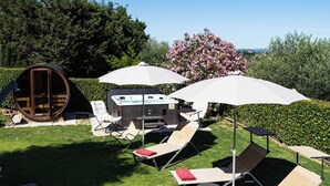 A pool area with lounge chairs, umbrellas, and a hot tub.
