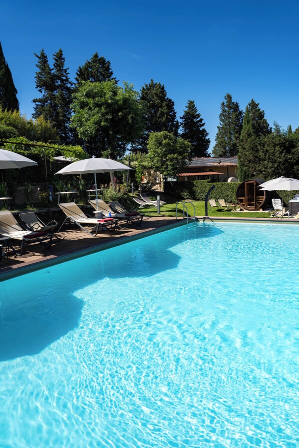 A swimming pool with lounge chairs and umbrellas, surrounded by trees and a building.