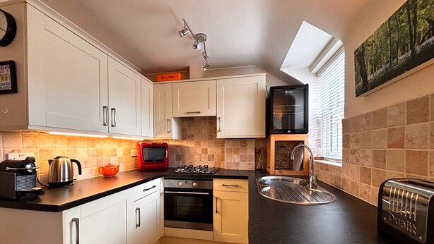 A modern kitchen with white cabinets, a gas stove, a built-in oven, a toaster, and a window with blinds.