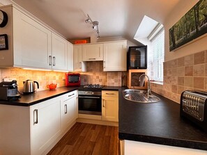 A modern kitchen with white cabinets, a gas stove, a built-in oven, a toaster, and a window with blinds.