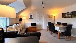 A compact living space with a sofa, a dining table with chairs, a TV, and a ceiling fan.