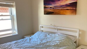 A bedroom with a bed, a nightstand, a window, and a painting on the wall.