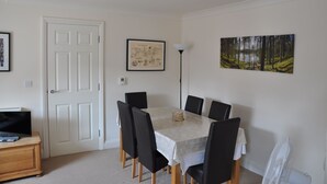 A dining area with a table and chairs, a lamp, a painting, and a door.