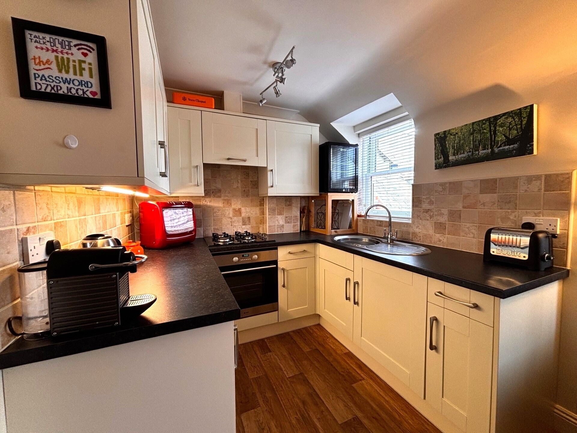 A modern kitchen with white cabinets, a black countertop, a stove, a sink, and a microwave.