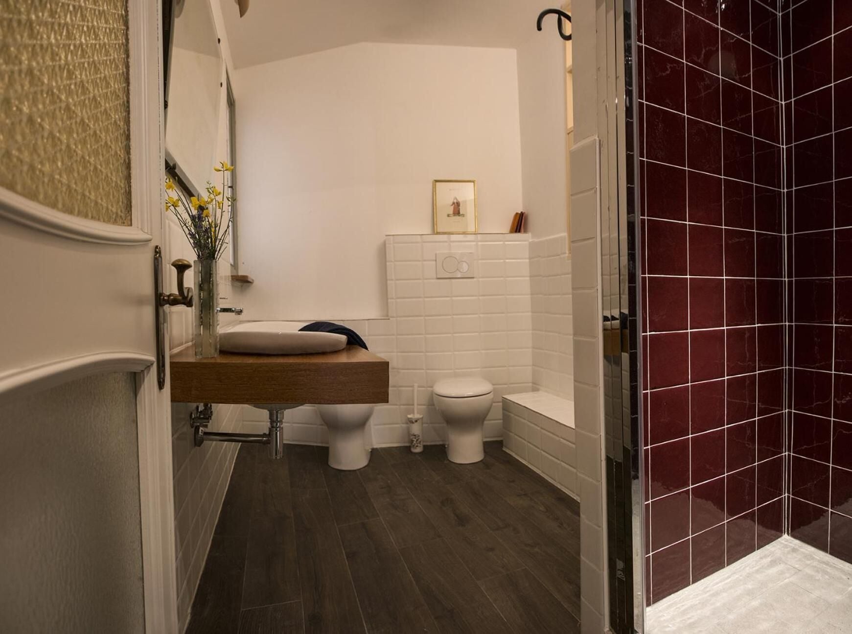 A modern bathroom with a wooden vanity, two toilets, and a shower area with dark tiles.