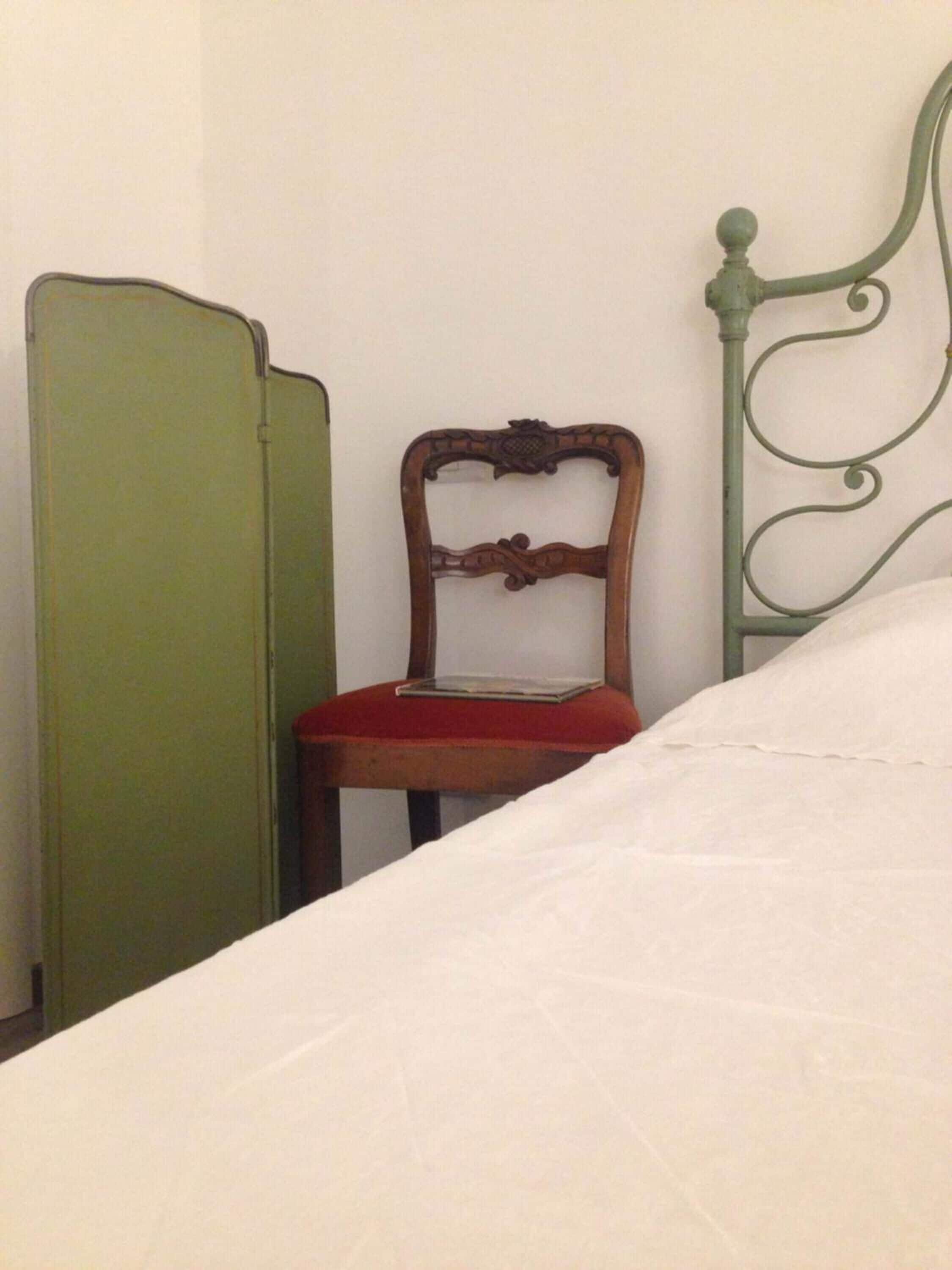 A bed with a white sheet, a wooden chair with a red cushion, and a green wardrobe.