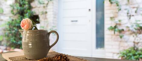 A ceramic pitcher with a single rose on a textured mat, placed on a wooden surface with pine cones.