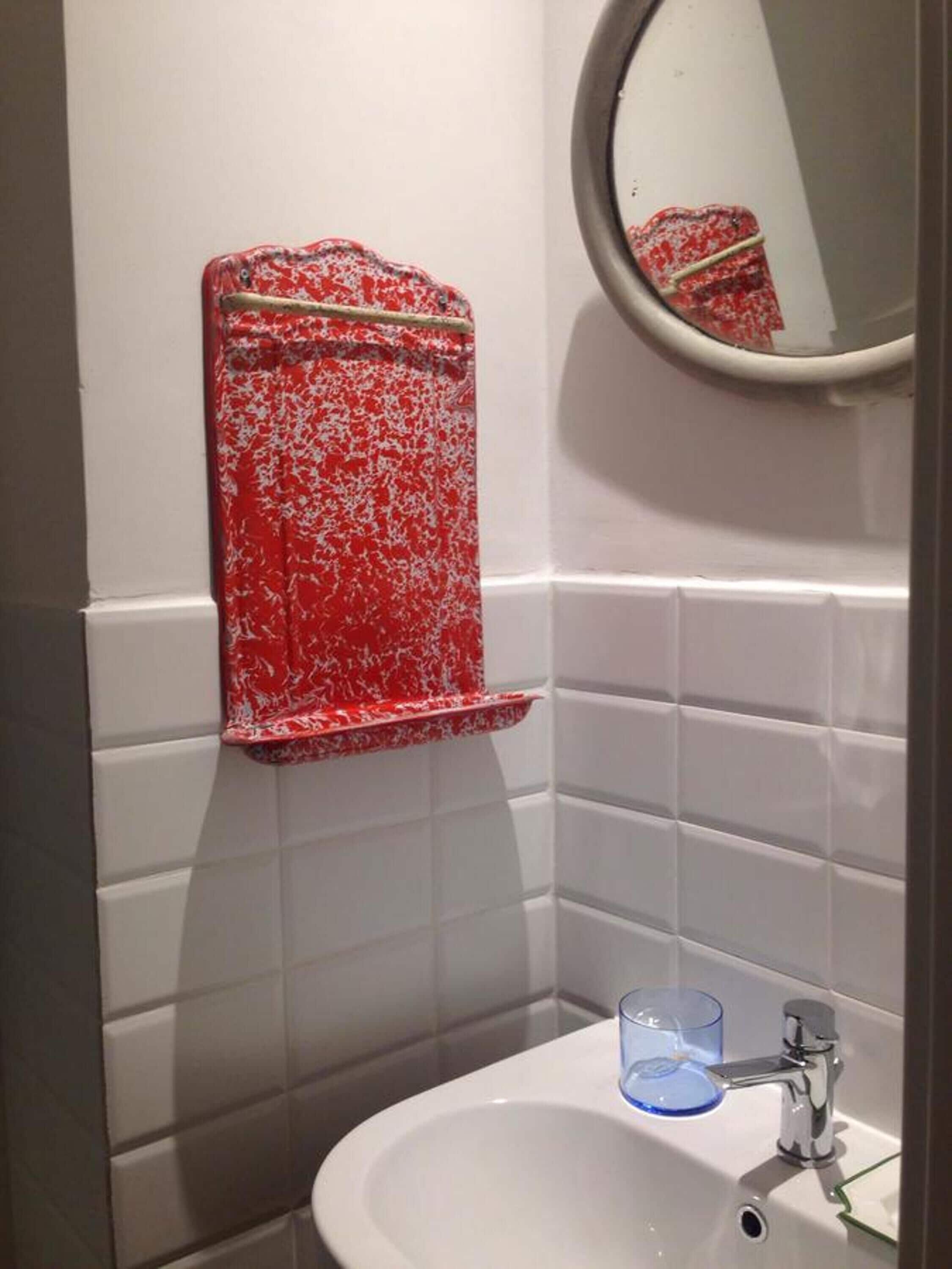 A bathroom with a white sink, a mirror, and a red towel warmer.