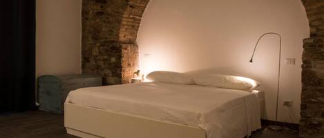 A bedroom with a large bed, a stone wall, and a modern lamp.