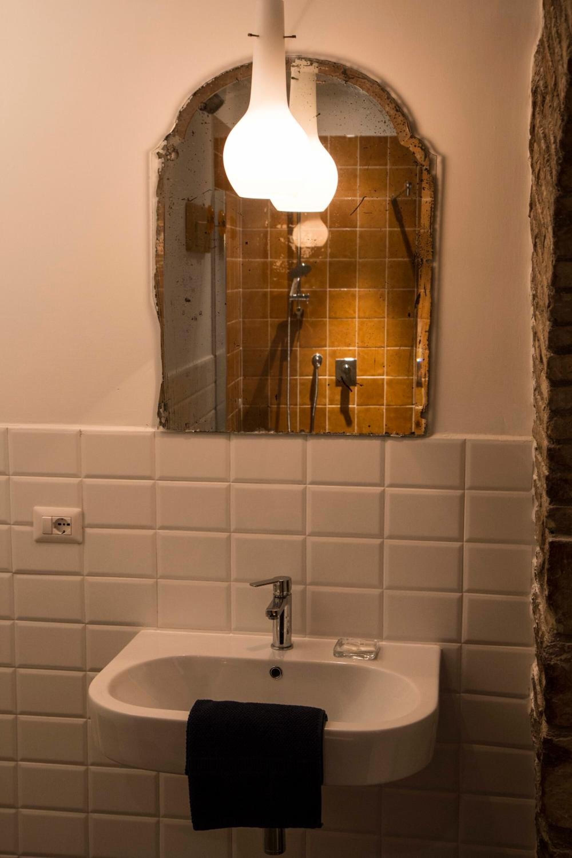 Une salle de bain avec un lavabo blanc, un miroir et un luminaire placé au-dessus du miroir.