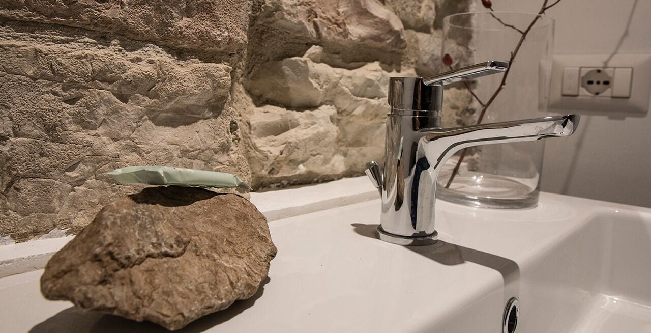A bathroom sink with a stone, a glass, and a faucet.