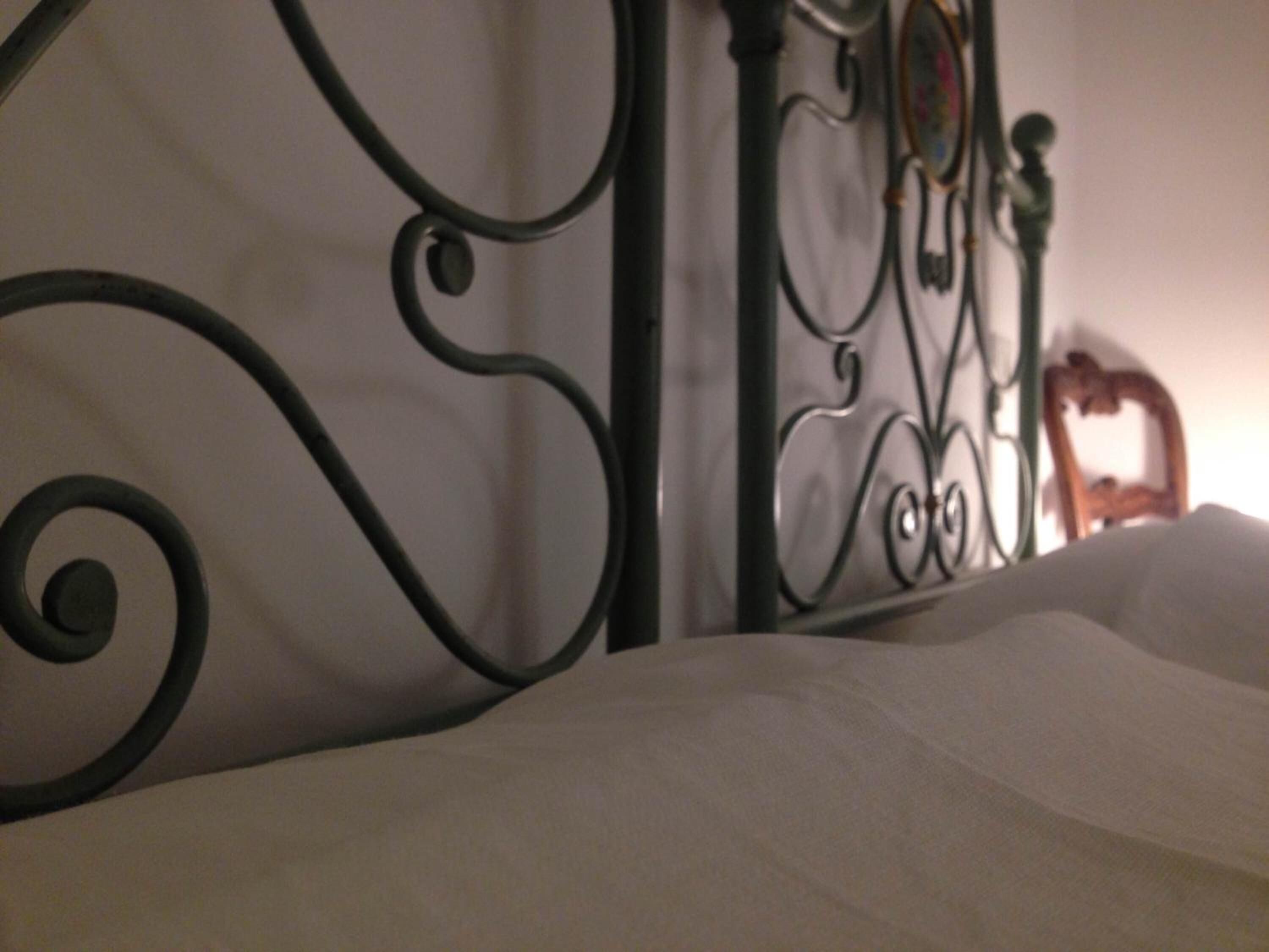 A bed with a metal headboard and a white sheet.