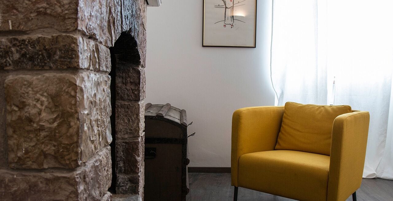 Una stanza con una parete in pietra, una poltrona gialla, un tavolino e un quadro incorniciato appeso al muro.