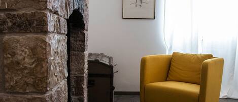 Una habitación con pared de piedra, un sillón amarillo, una mesita y un cuadro enmarcado en la pared.