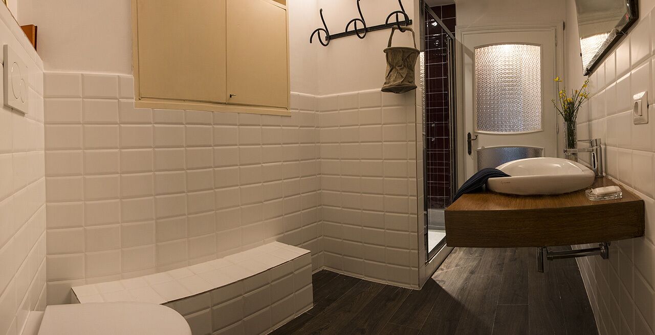 A bathroom with white subway tiles, a wooden vanity, a white sink, and a shower area.